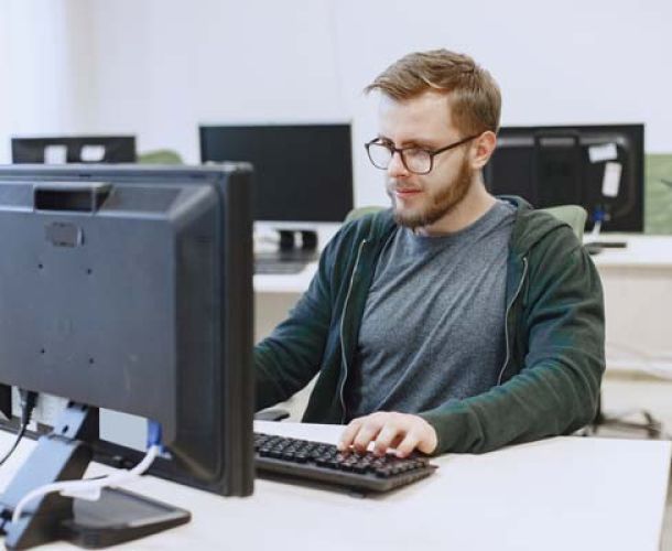 A man wearing glasses is focused on typing on a laptop computer.