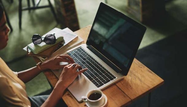 A woman focused on her laptop, typing intently with a thoughtful expression.  