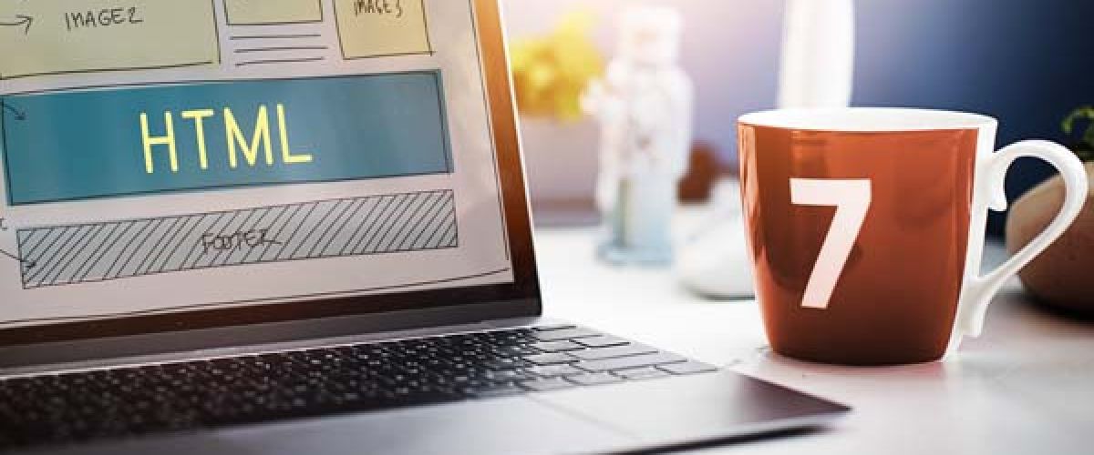 A coffee mug beside a laptop displaying the HTML  logo on the screen, suggesting a coding or web development environment.
