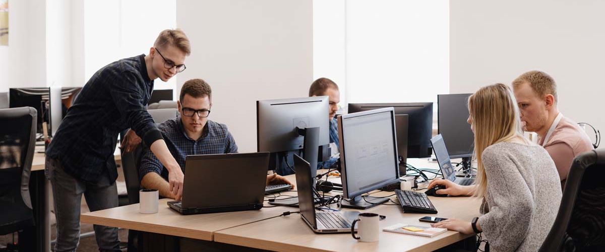 A diverse group of professionals collaborating at computers in a modern office environment. 