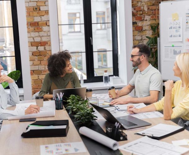 A group of diverse individuals engaged in discussion around a conference table in a modern office setting.