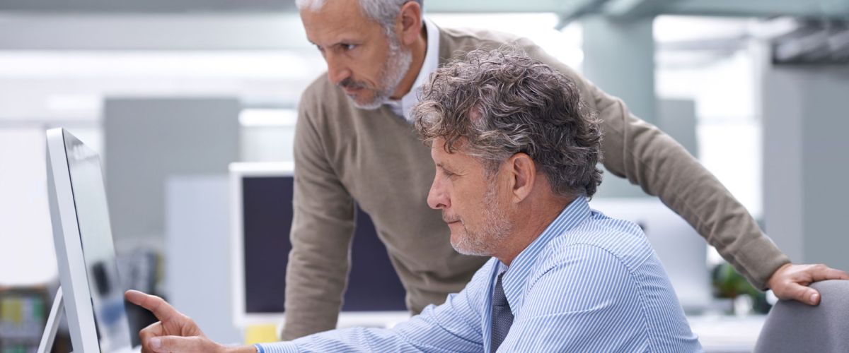 An older man sitting at a desk, engaged in a conversation