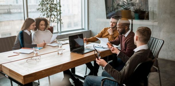 A group of five people engaged in discussion around a conference table in a modern office setting. 