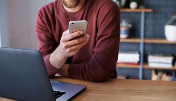 A man sits at a table, working on a laptop with a cell phone beside him.