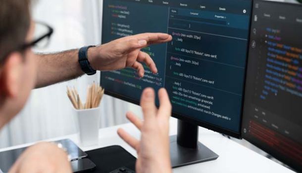  A man points at a computer screen displaying lines of code, indicating a focus on programming or software development.  