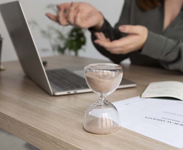 A woman in a business suit is focused on her laptop, working diligently in a professional setting next to a hourglass.