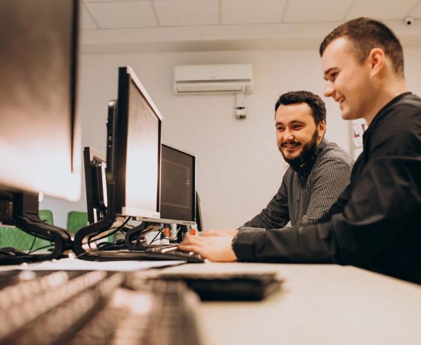 Two men collaborating on computers in a modern office setting, focused on their work. 