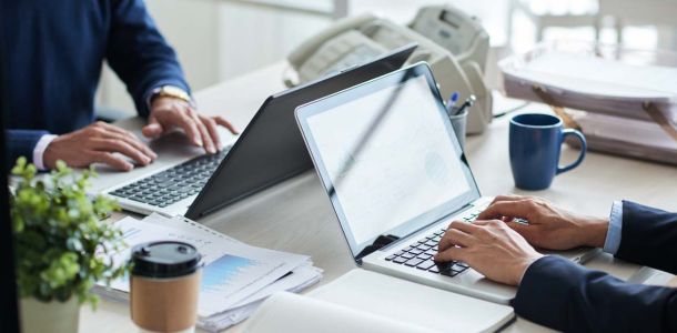  Two individuals focused on their laptops while collaborating at a shared desk in a modern workspace.  