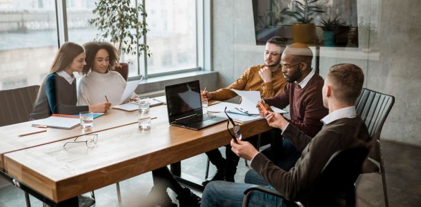 A group of five people engaged in discussion around a conference table in a modern office setting. 